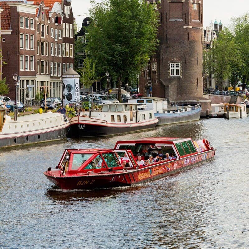 City Sightseeing Hop-on Hop-off by boat in Amsterdam on the water with houses and tower on the background